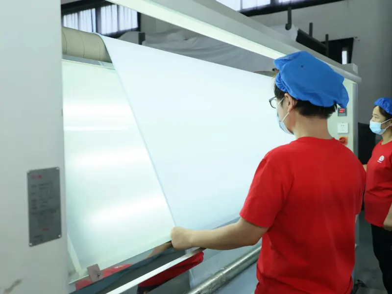 Incoming material QC personnel visually checking the raw fabric surface under illumination