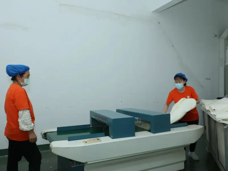 A finished sewn bedding product being placed onto the needle detector conveyor before packing