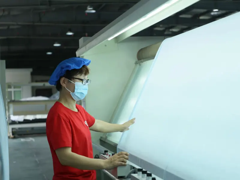 Incoming material QC personnel closely observing the fabric surface under inspection lighting