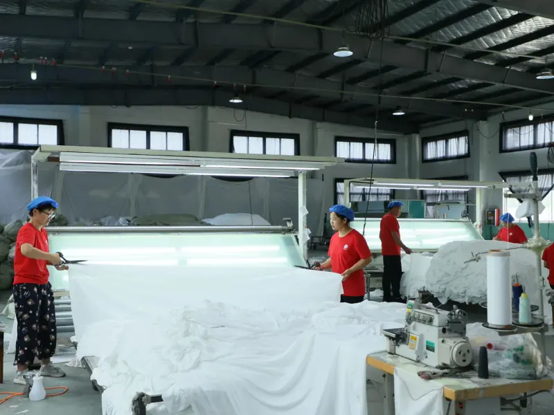 Incoming material QC personnel spreading fabric across illuminated inspection tables for visible review